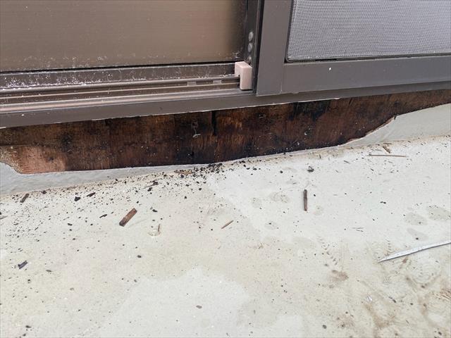 掃出し窓の外、下の壁が剥がされて中が覗く。雨漏りのため黒ずんでいる。
