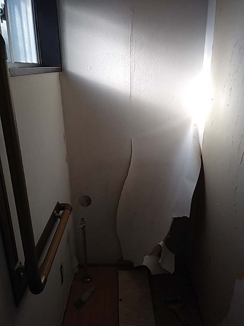 光が反射したトイレ個室内、壁紙が剥がれている