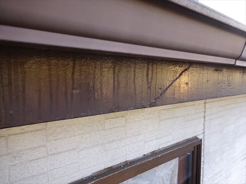 外壁の一部、上から雨樋、破風板、外壁、窓と並ぶ。破風板に亀裂と雨垂れの跡がある