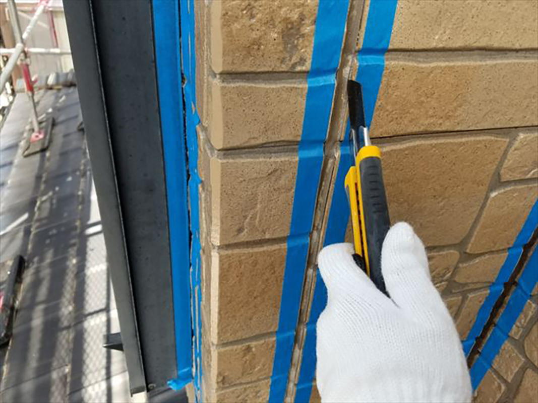 カッターなどで 古く固くなったコーキングを除去します。     青いテープは 養生用です。  溝の両側の壁を傷付けたり 塗りこむ材料がはみ出して着いたりしないようにする為に貼っています。