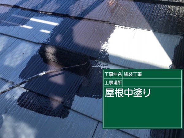 スレート屋根塗装中塗り、上塗り塗料を塗って下塗りで白っぽくなった屋根が黒く塗られている様子