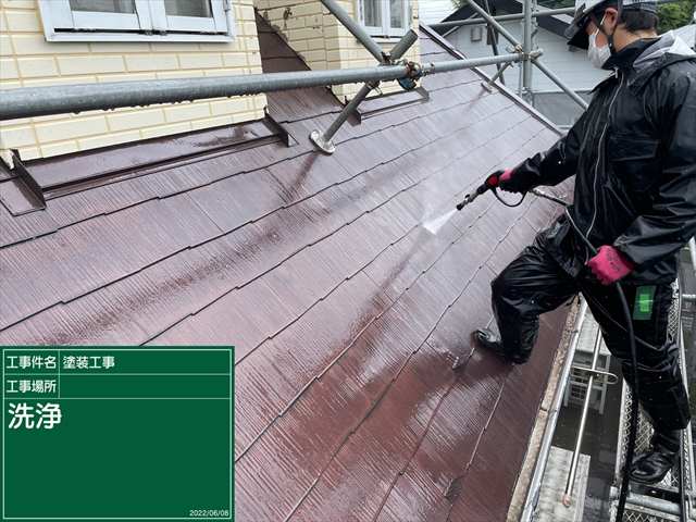 足場から屋根に足をかけて高圧洗浄機で屋根の汚れを落とす様子